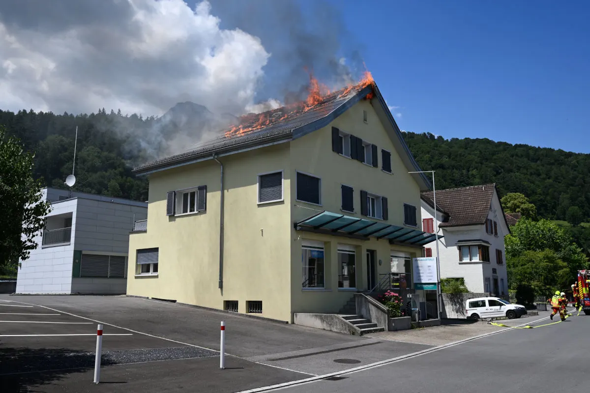 Ein zweigeschossiges Gebäude steht in Flammen; Rauch steigt vom Dach auf. Die Feuerwehr ist vor Ort.