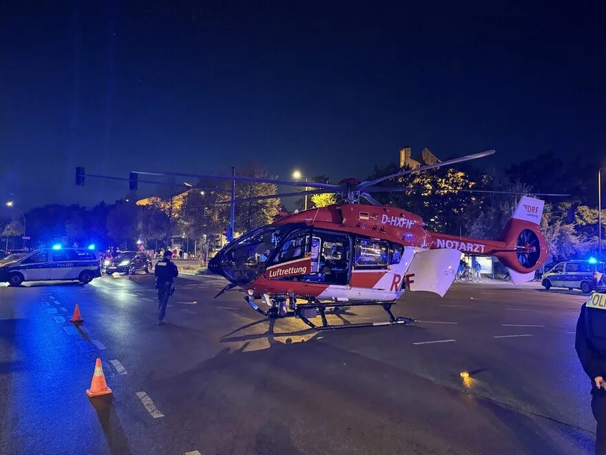 Ein roter Rettungshubschrauber der Luftrettung steht bei Nacht auf einer beleuchteten Straße mit mehreren Polizeifahrzeugen im Hintergrund.