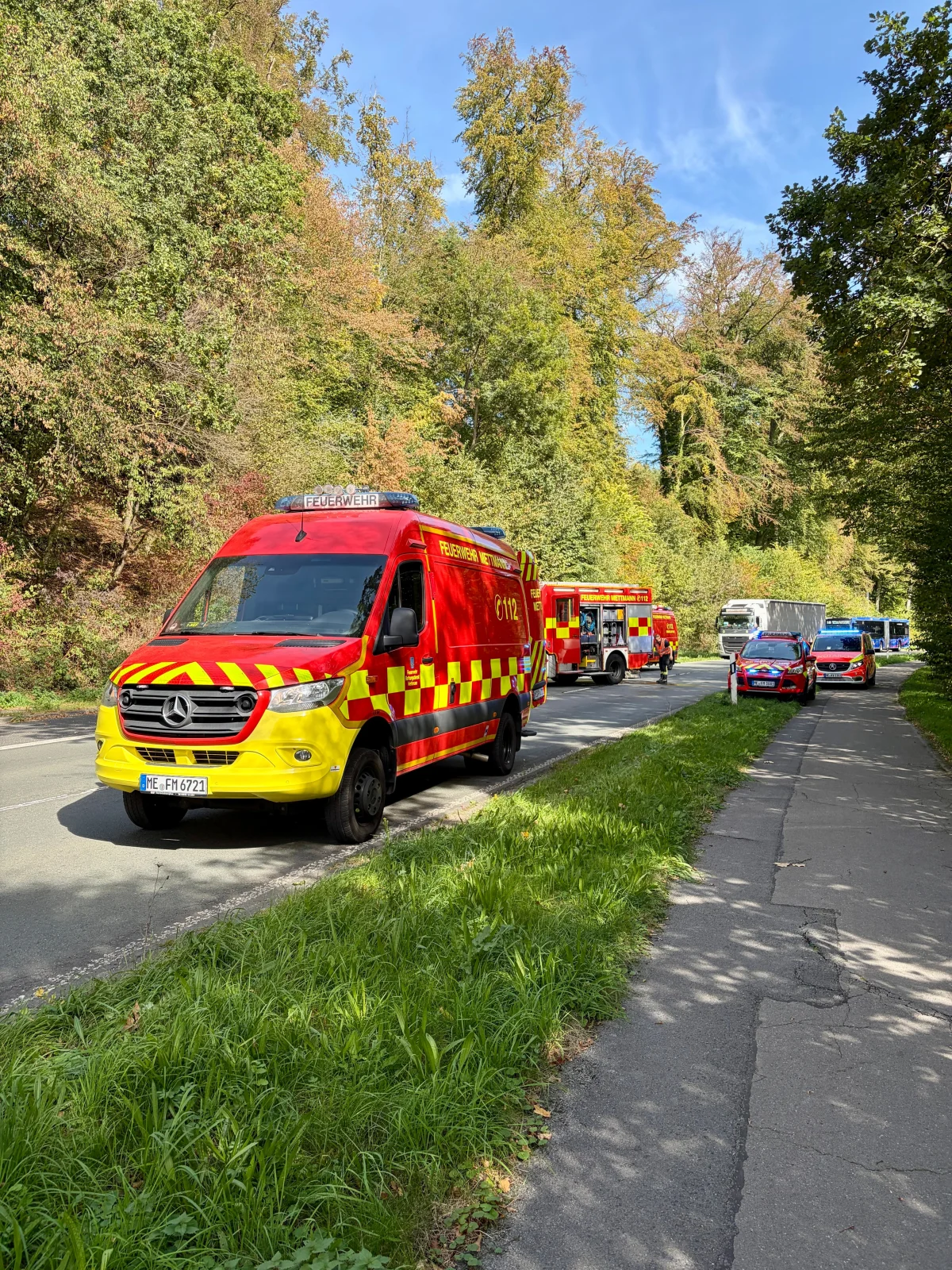 Mehrere rote Feuerwehrfahrzeuge parken auf einer Straße, umgeben von herbstlichen Bäumen. Feuerwehrkräfte sind nicht sichtbar.