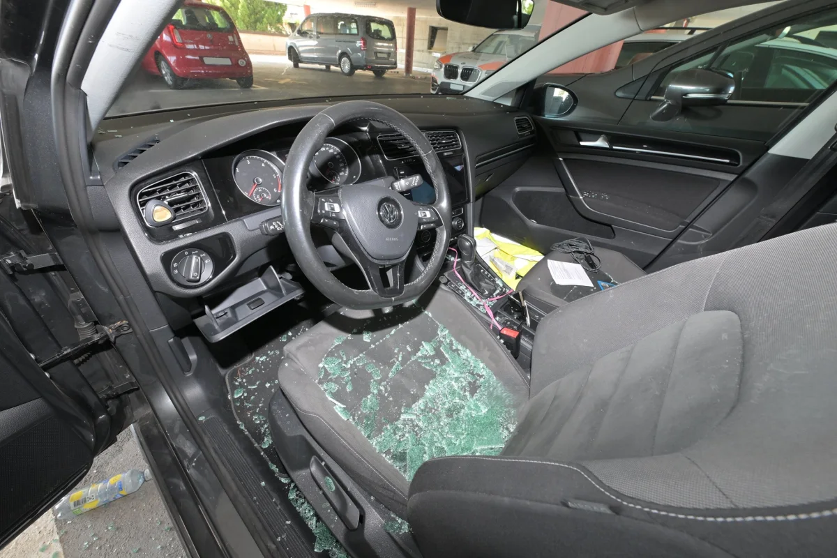 Das Bild zeigt den Innenraum eines Autos. Auf dem Sitz ist zerbrochenes Glas verstreut, das offenbar von einer beschädigten Scheibe stammt.