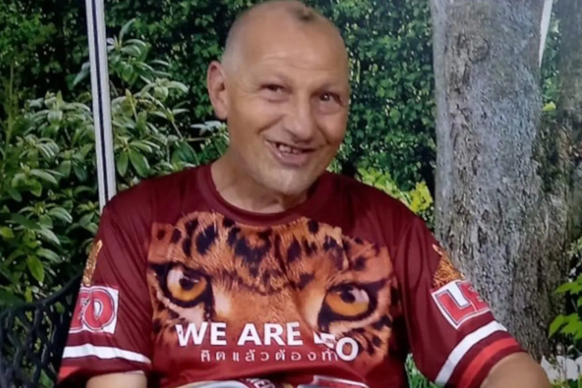 Ein älterer Mann im roten T-Shirt mit einem Tigeraufdruck sitzt vor einer Kulisse aus dichtem Buschwerk.