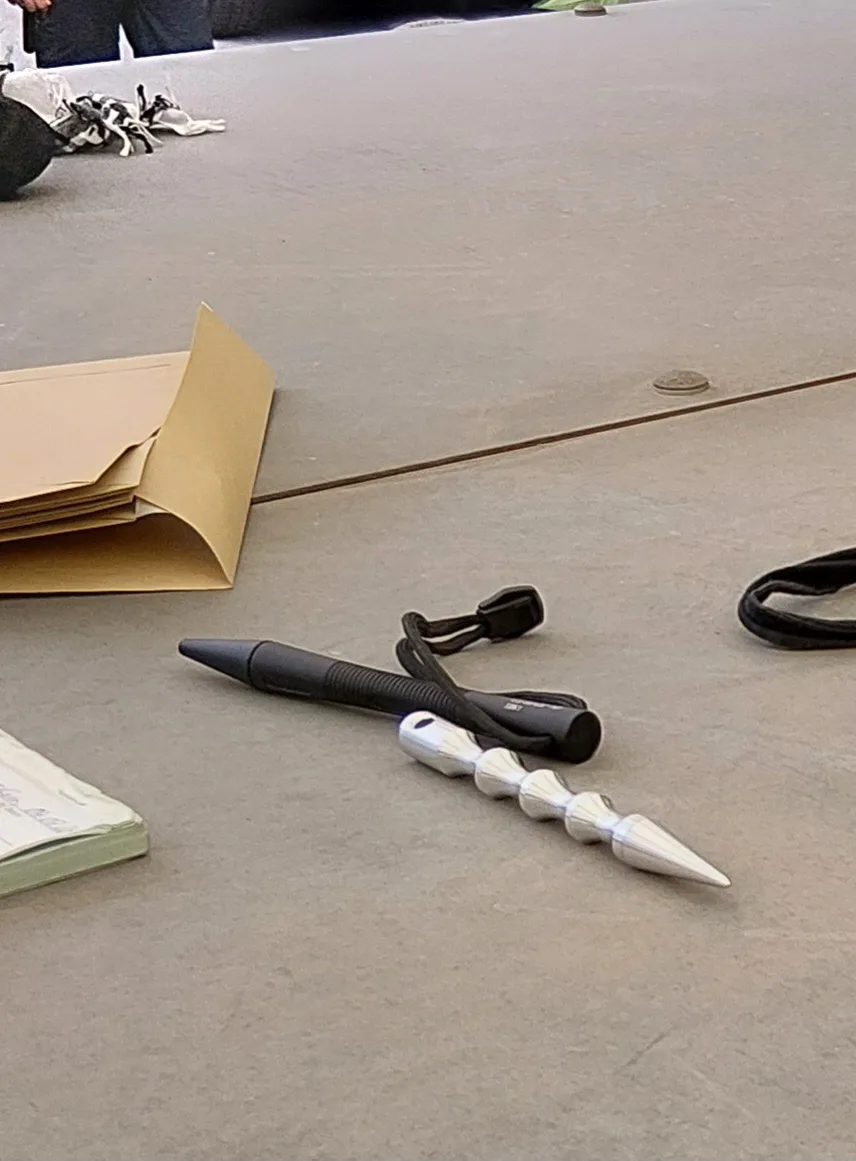 Auf einem Tisch liegen ein geöffneter Ordner, ein schwarzer Stift und ein ungewöhnliches hölzernes Werkzeug mit Spitzen.