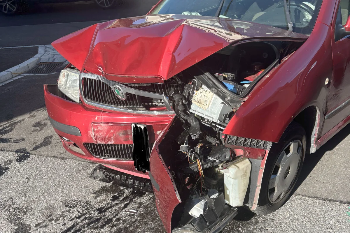 Die Front eines roten Škoda ist stark beschädigt nach einem Unfall, mit sichtbarem, verzogenem Blech und offenen Motorteilen.