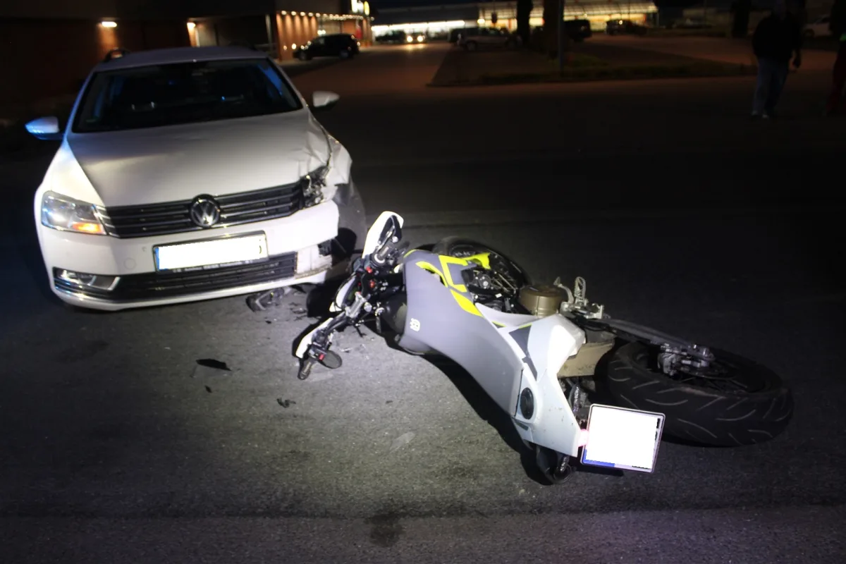 Ein weißes Auto hat auf einer nächtlichen Straße ein gestürztes Motorrad getroffen. Beide Fahrzeuge sind beschädigt.