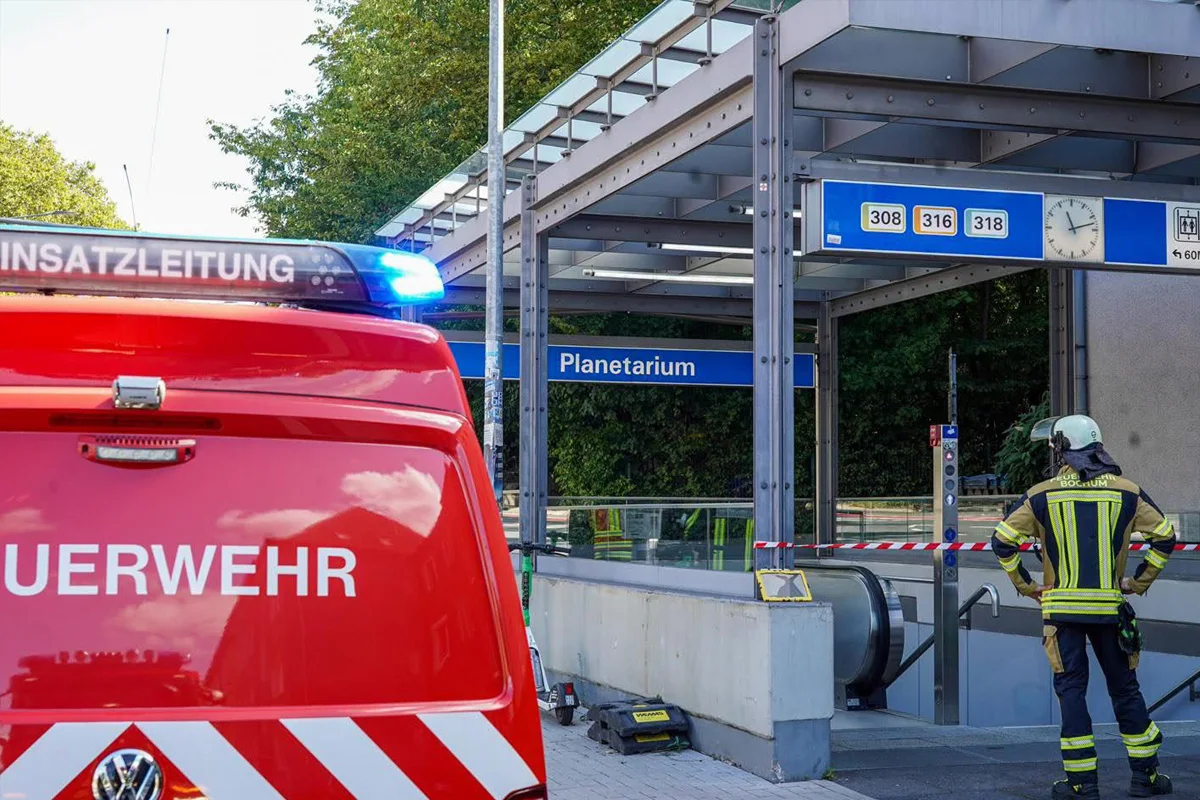 Ein rotes Feuerwehrfahrzeug mit Blaulicht steht vor einem U-Bahn-Eingang. Ein Feuerwehrmann in Schutzkleidung steht daneben.