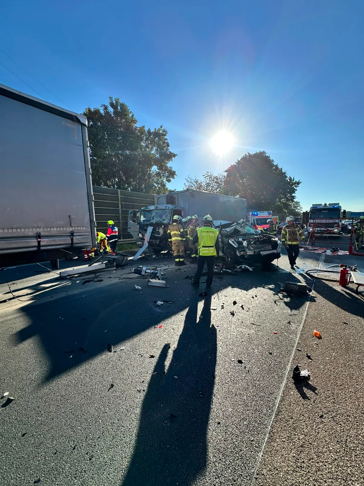 Auf der Autobahn stehen mehrere Einsatzkräfte um ein zerstörtes Fahrzeug. Trümmerteile sind auf der Straße verteilt.