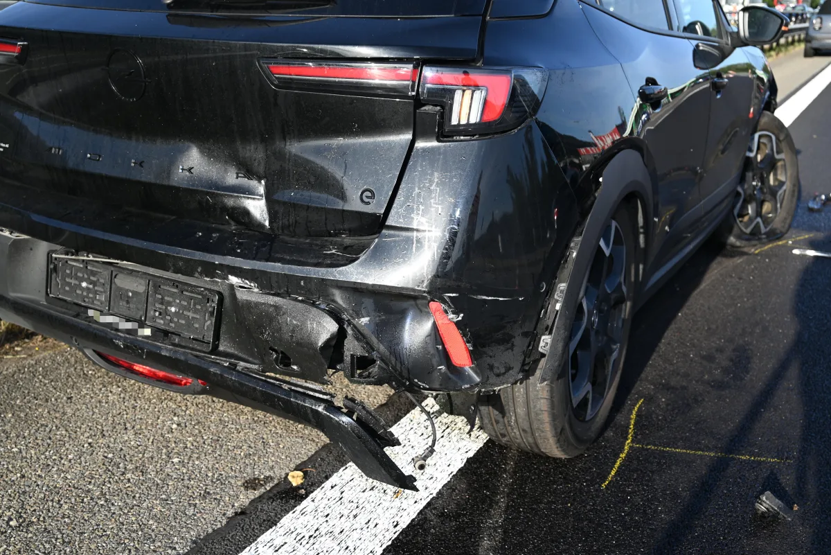 Das Bild zeigt die Rückseite eines beschädigten schwarzen Autos auf einer Straße. Der hintere Stoßfänger und die Karosserie sind eingedellt, was auf einen Unfall hindeutet.