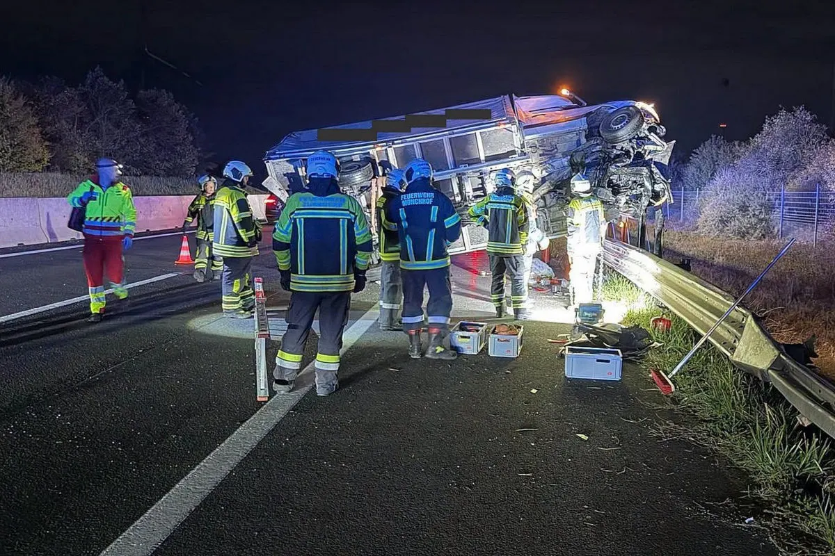 Mehrere Feuerwehrleute arbeiten an einem umgekippten Transporter auf der Autobahn bei Nacht. Ausrüstung ist verstreut auf der Straße.