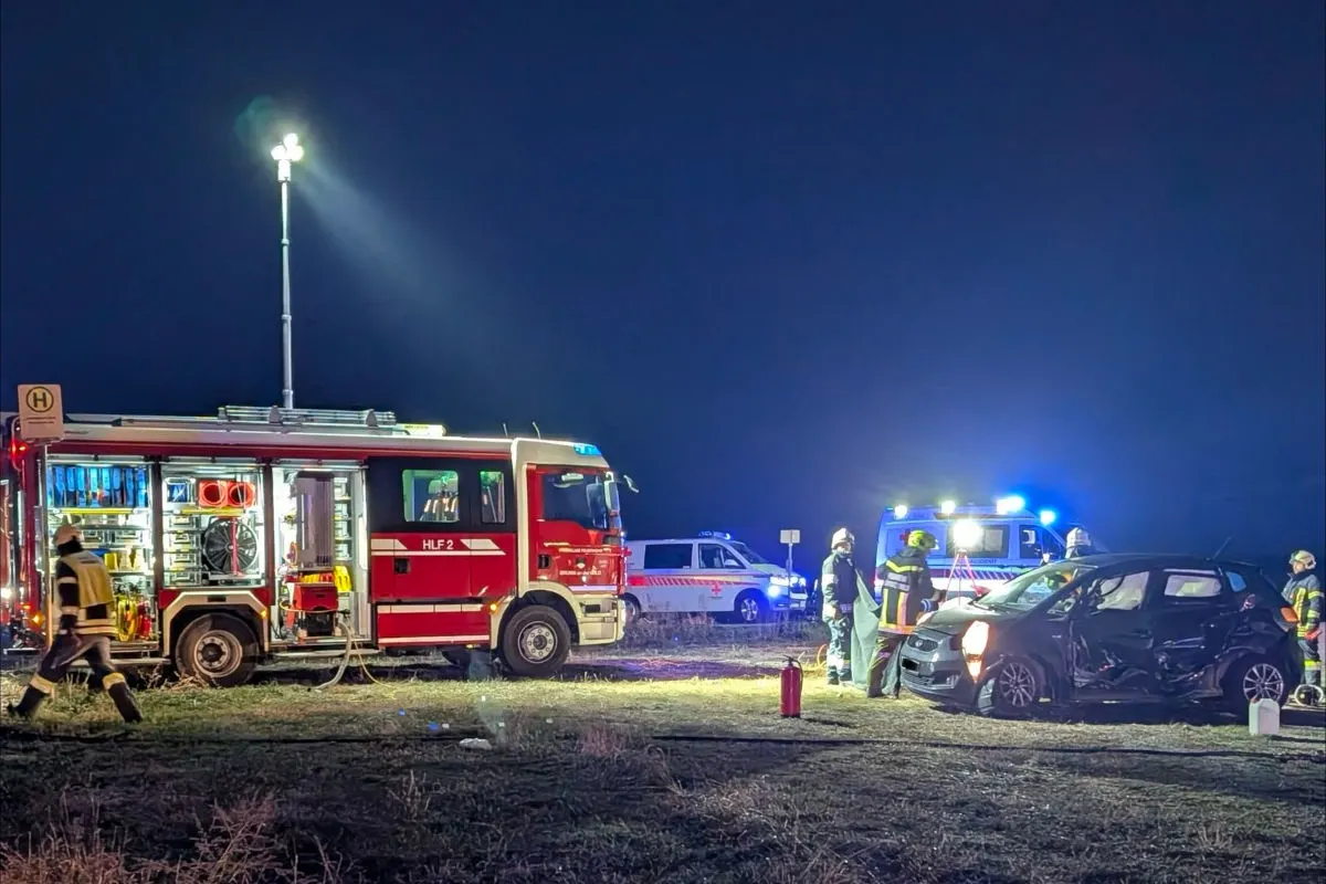 Ein Feuerwehrfahrzeug und Polizeiwagen stehen bei Nacht im Einsatz. Feuerwehrleute arbeiten an einem beschädigten Auto.