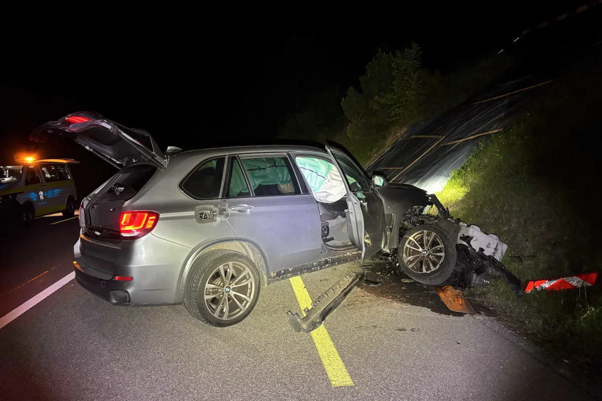 Ein grauer BMW SUV steht stark beschädigt auf einer nächtlichen Autobahn. Die Türen sind geöffnet, und die Front ist deformiert.