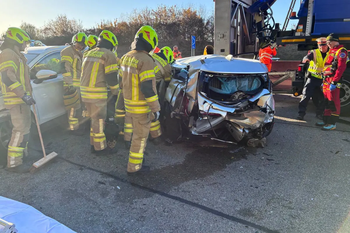 Mehrere Feuerwehrleute stehen um ein stark beschädigtes Auto auf der Straße. Ein Lkw ist im Hintergrund sichtbar.