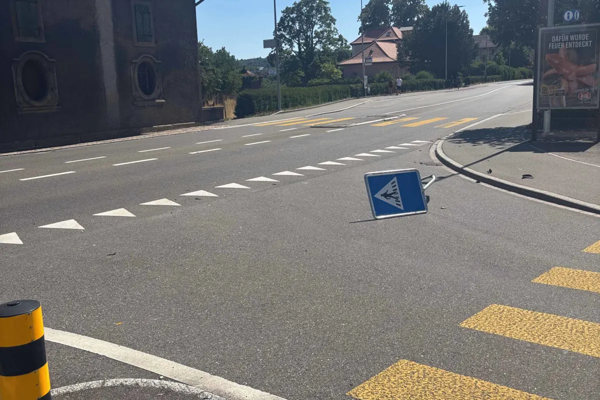 Ein umgestürztes Verkehrsschild liegt auf einer asphaltierten Straße. Im Hintergrund sind Gebäude und Vegetation zu sehen.