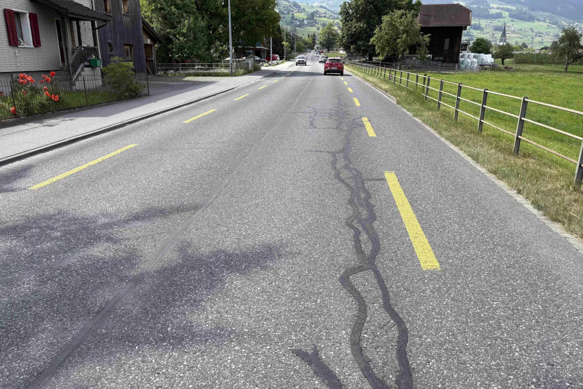 Eine ländliche Straße mit einem roten Auto fährt auf einem klaren Sommertag durch eine Schweizer Landschaft.