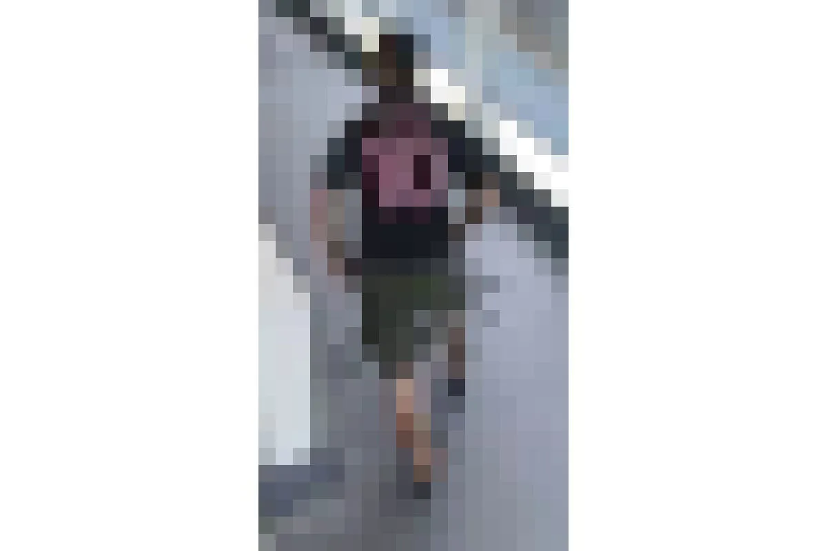 Eine Person in einem dunklen T-Shirt mit einem großen Motiv auf dem Rücken und Shorts steht auf einem Gehweg; der Kopf ist nicht erkennbar.