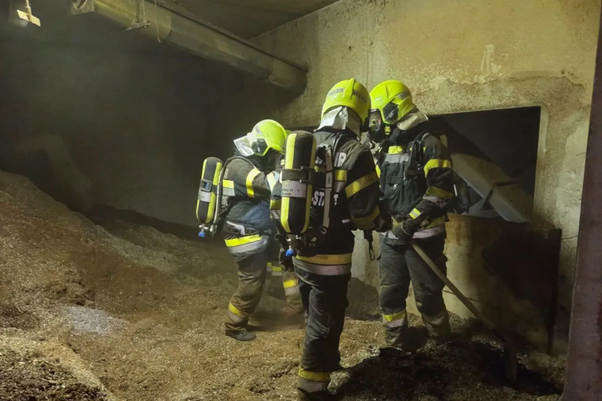 Drei Feuerwehrleute in Schutzanzug stehen in einem staubigen Raum. Sie tragen Atemschutzgeräte und sind im Einsatz.