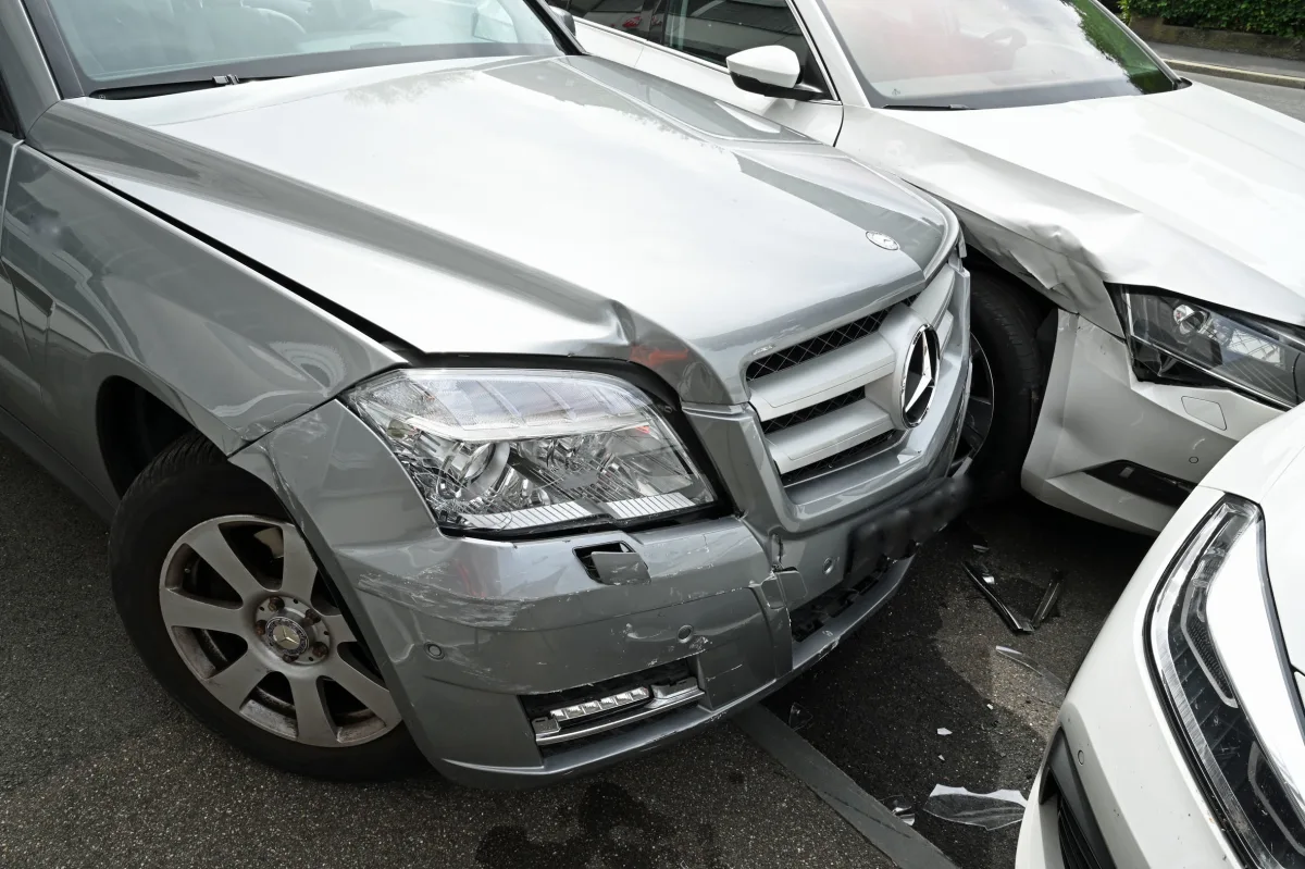 Ein grauer Mercedes mit beschädigter Front steht eng neben einem weißen Audi, der ebenfalls Unfallschäden zeigt. Beide Fahrzeuge haben sichtbare Schäden an den Stoßstangen und Kotflügeln.