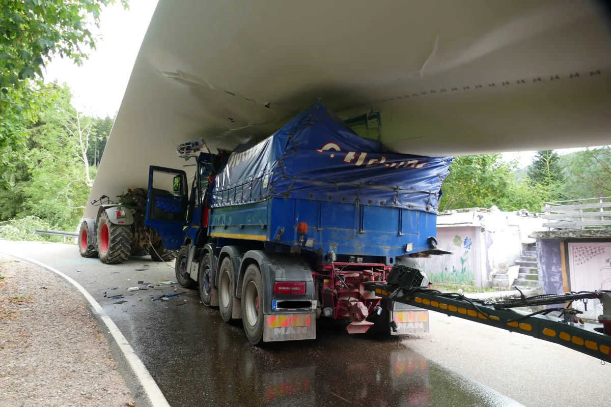 Ein blauer Lkw mit Planenaufbau klemmt unter einer niedrigen Brücke. Ein Traktor ist ebenfalls beteiligt.
