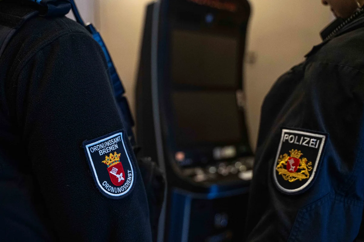 Im Vordergrund sind zwei Personen in Uniform zu sehen, die Polizei- und Ordnungsdienstabzeichen von Bremen tragen. Im Hintergrund steht ein Automat.