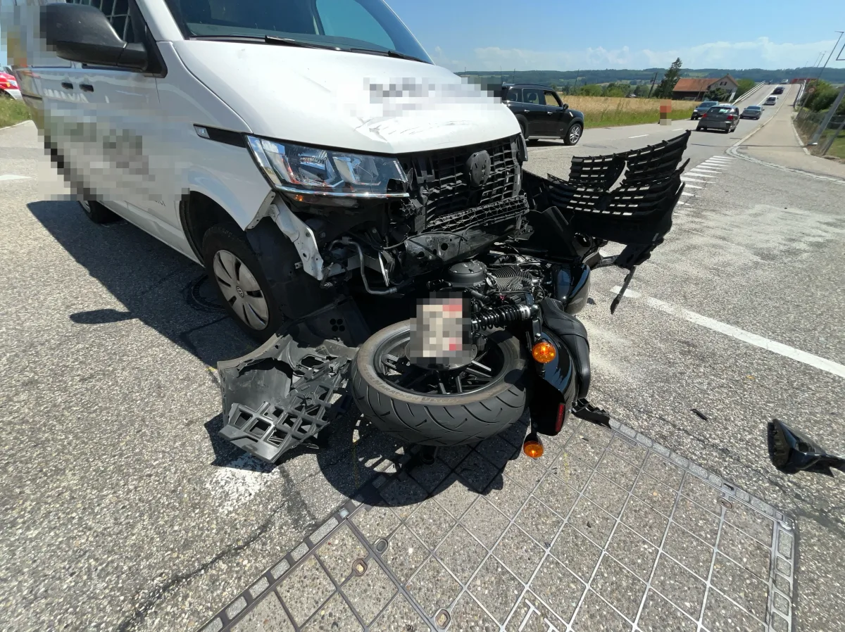 Ein weißer Van mit erheblichen Frontschäden steht hinter einem umgestürzten Motorrad auf einer Landstraße. Der Unfall ereignete sich bei klarem Wetter.