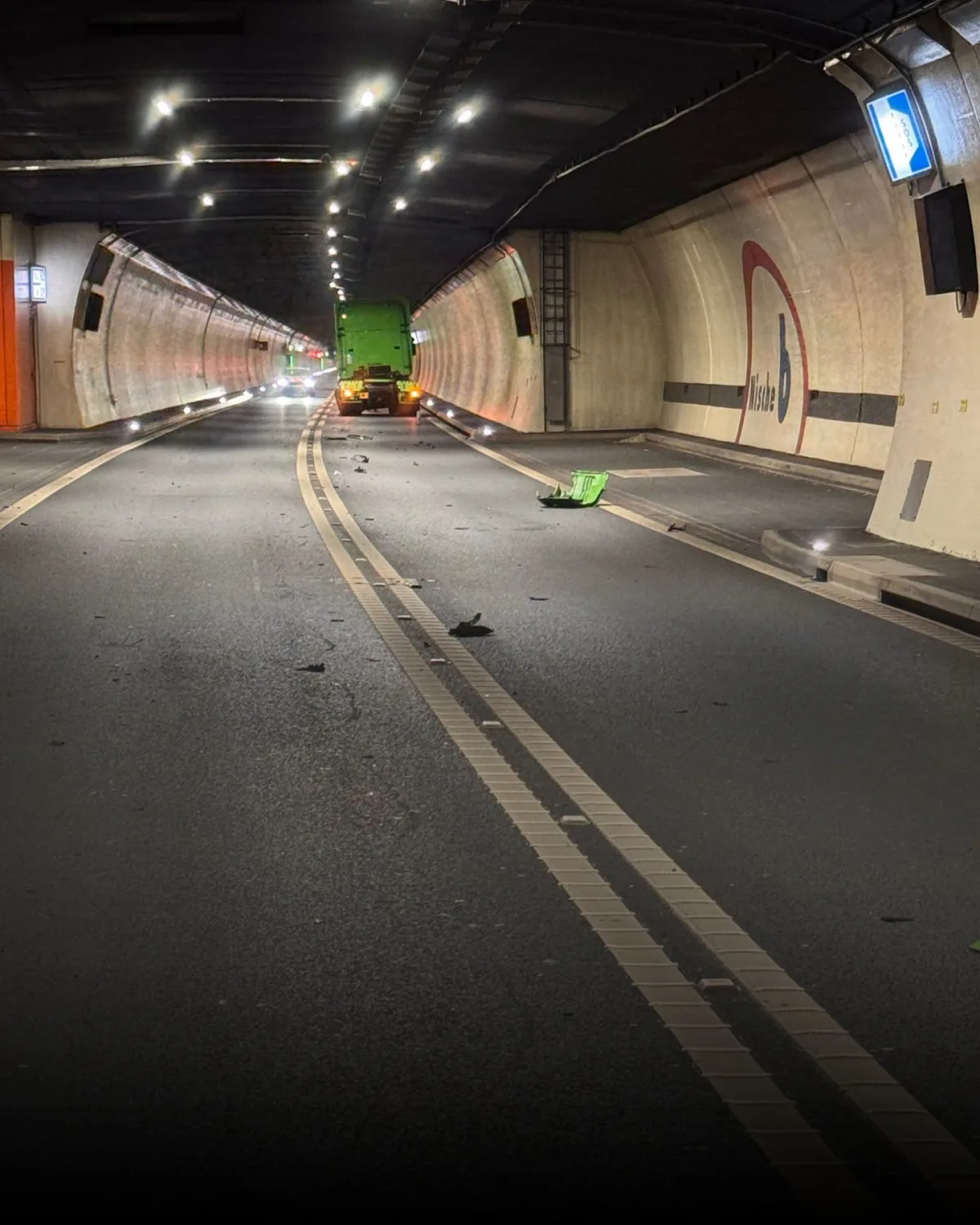 In einem Tunnel fährt ein grüner Lastwagen, während diverse Trümmer auf der Fahrbahn liegen. Die Beleuchtung ist künstlich und der Tunnel ist leer, bis auf den Lastwagen und die Trümmer.