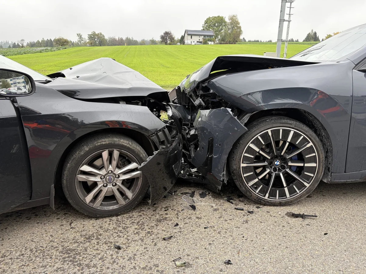 Zwei Fahrzeuge sind frontal ineinander gefahren, wodurch beide Fronten stark beschädigt wurden. Die Aufnahme zeigt die Szene auf einer Landstraße mit einem grünen Feld im Hintergrund.