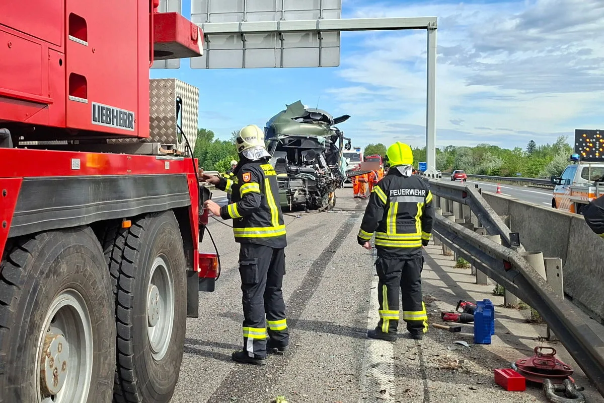 Auf der Autobahn ist ein schwer beschädigtes Fahrzeug zu sehen. Feuerwehrleute stehen daneben, um Hilfe zu leisten.