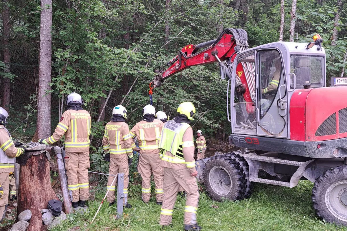 Mehrere Feuerwehrleute in Schutzkleidung arbeiten im Wald mit einem Bagger, um eine Einsatzstelle zu sichern.