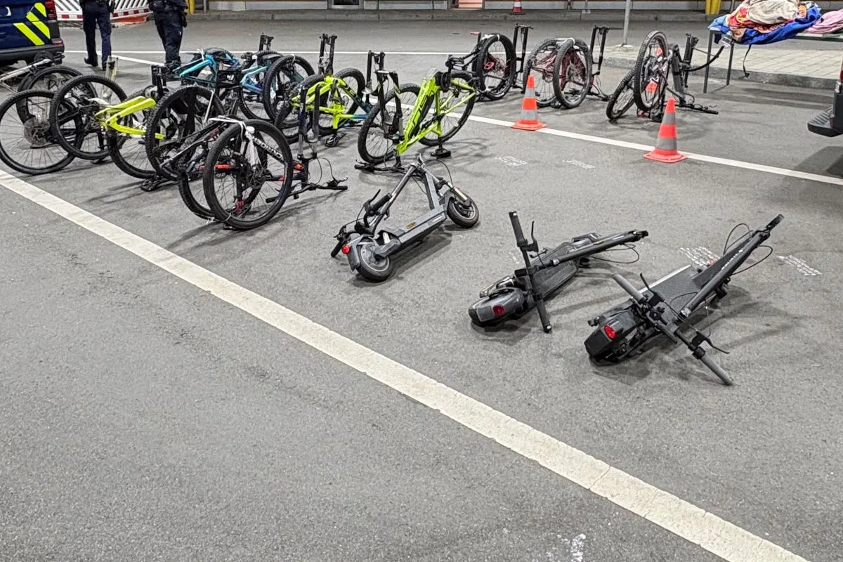 Mehrere E-Roller und Fahrräder liegen und stehen auf einem Parkplatz, gesichert durch orangefarbene Verkehrskegel.