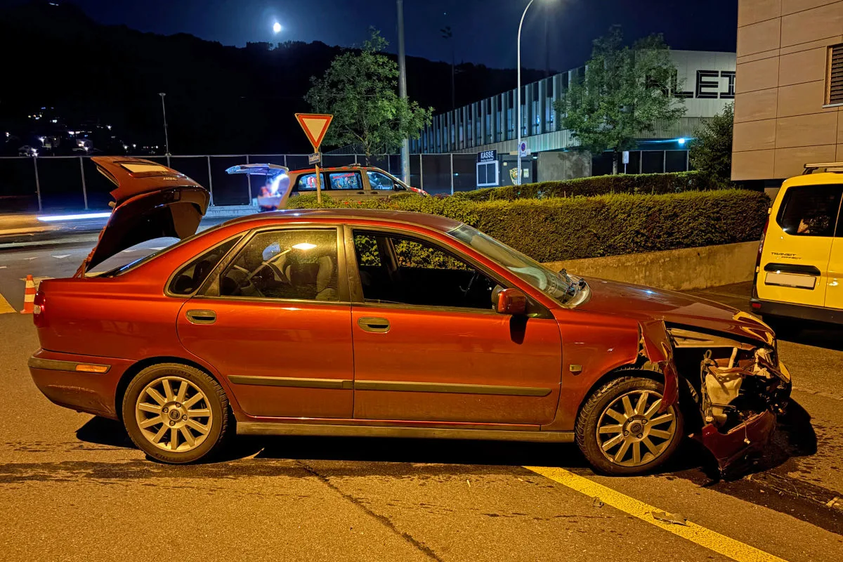 Bei Nacht steht ein rotes Auto mit stark beschädigter Front am Straßenrand. Das Auto hat den Kofferraum offen.