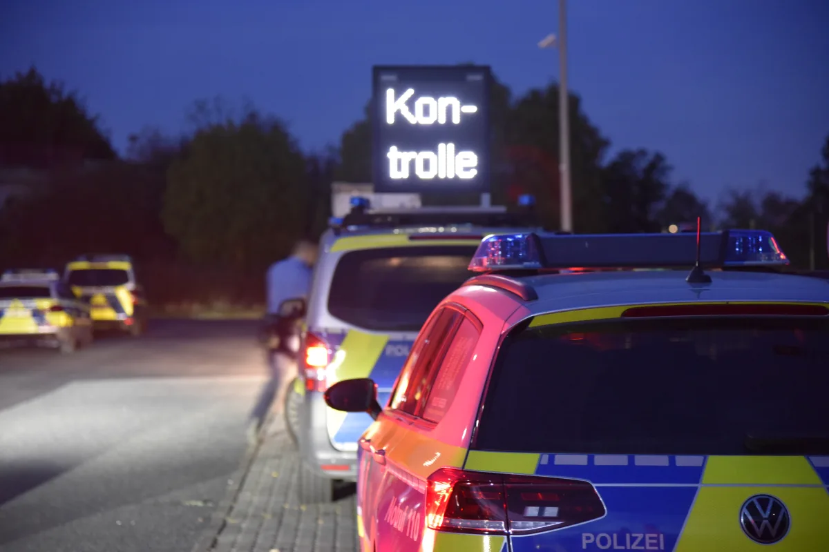 Mehrere deutsche Polizeifahrzeuge stehen in der Dämmerung auf einer Straße. Eine elektronische Anzeige zeigt 'Kontrolle'.