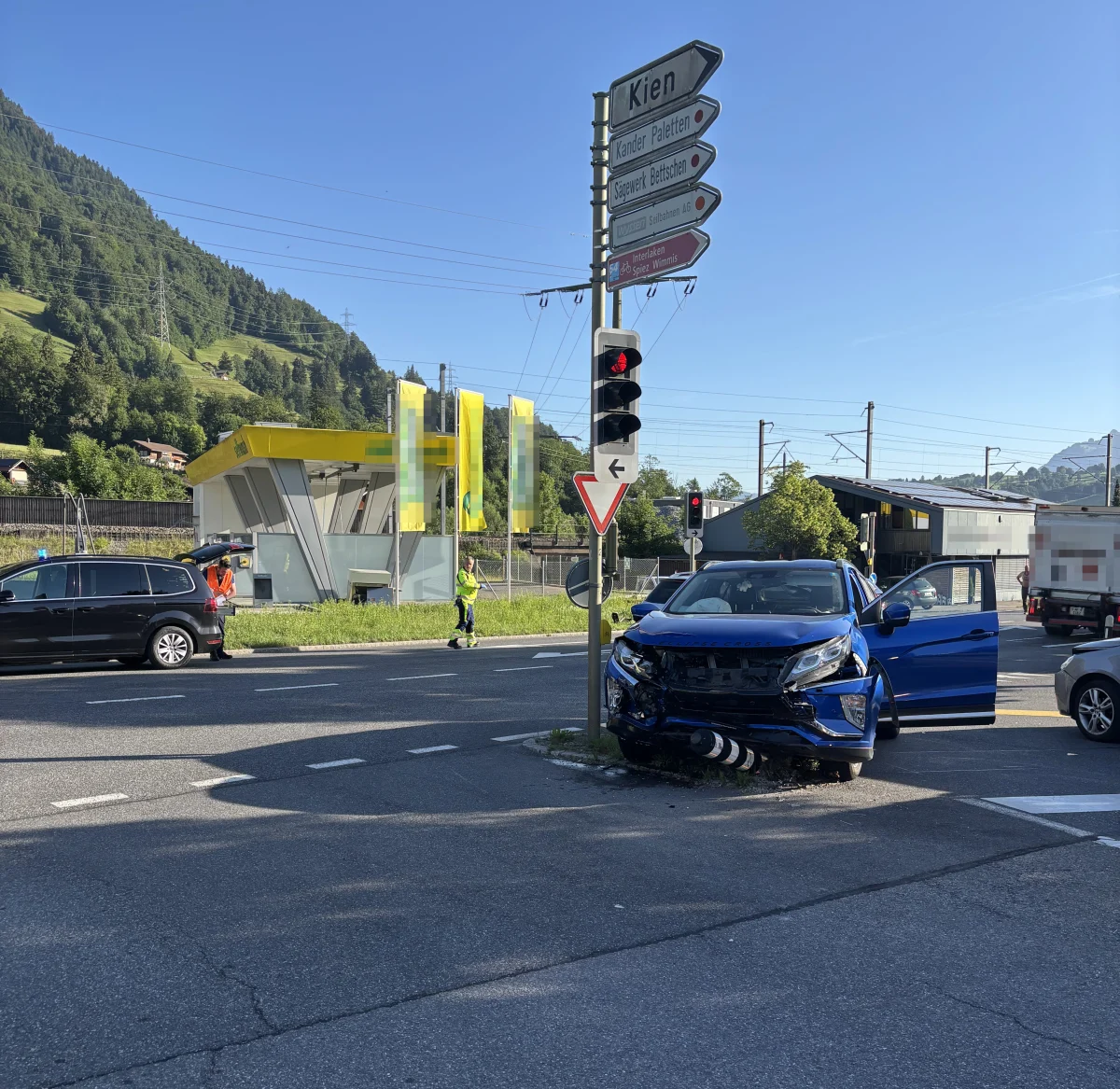 Ein blauer SUV steht mit beschädigter Front an einem Ampelmast. Im Hintergrund ist eine Tankstelle zu sehen.