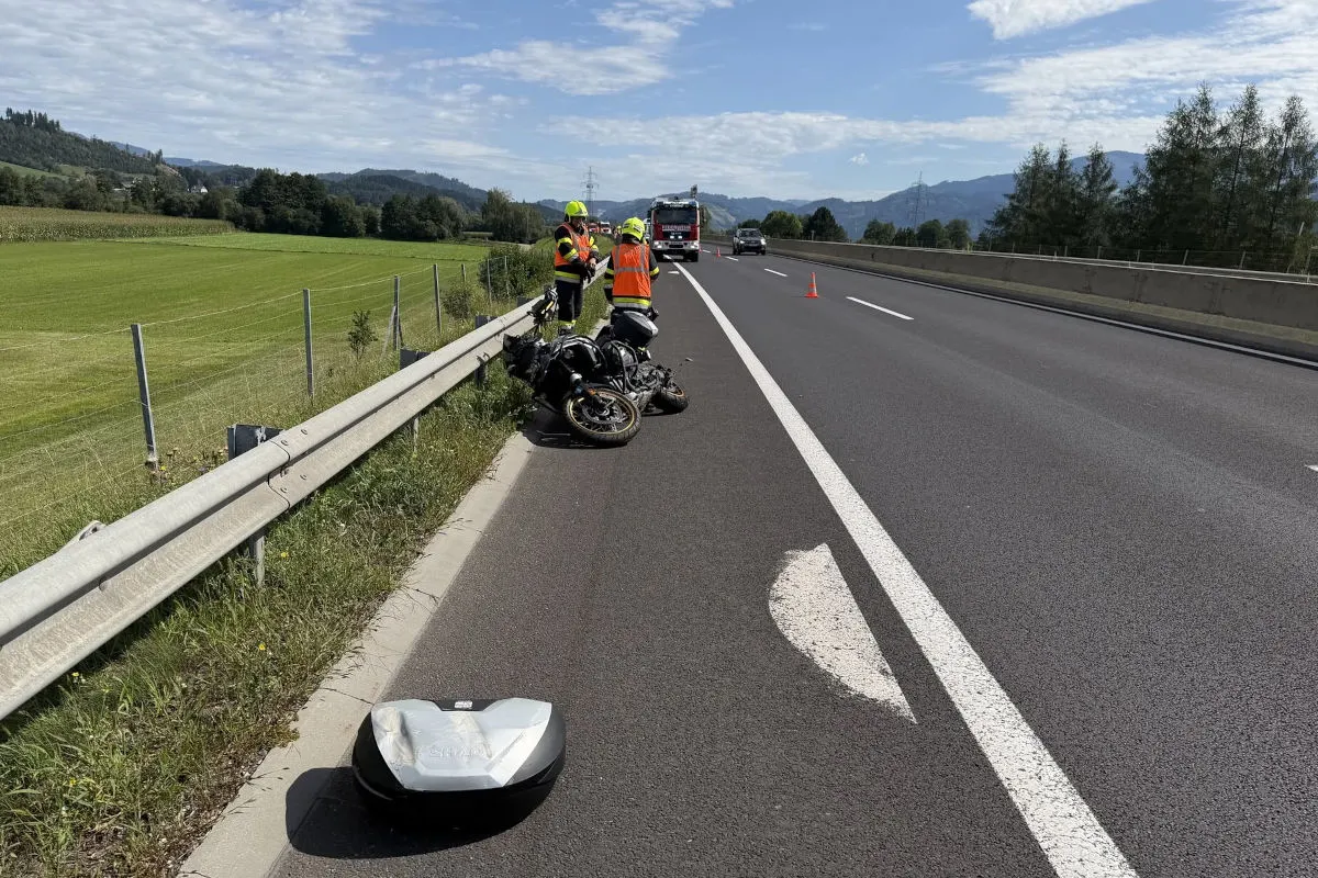 Ein verunglücktes Motorrad liegt an der Leitplanke einer Landstraße. Feuerwehrleute tragen Schutzwesten und sichern die Unfallstelle. Im Hintergrund ist ein Einsatzfahrzeug sichtbar.