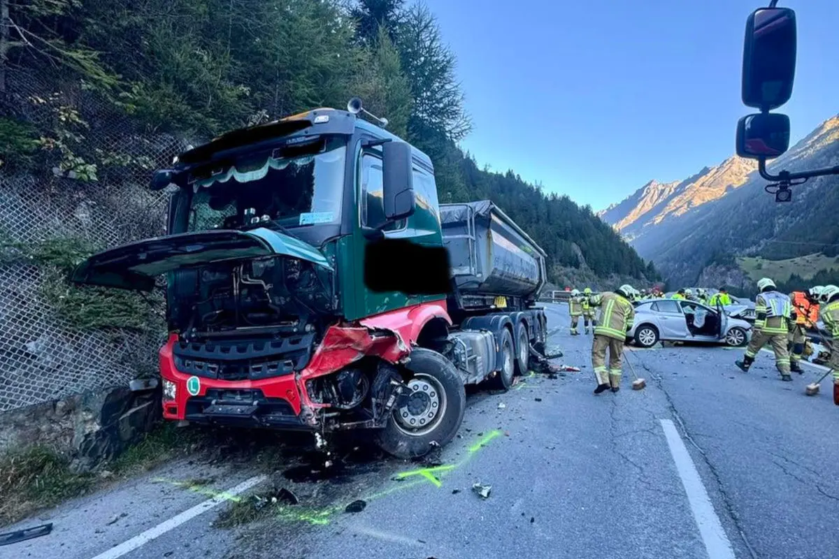 Ein stark beschädigter Lastwagen steht auf einer Straße in den Bergen. Feuerwehrleute sichern die Unfallstelle, während im Hintergrund ein Pkw zu sehen ist.