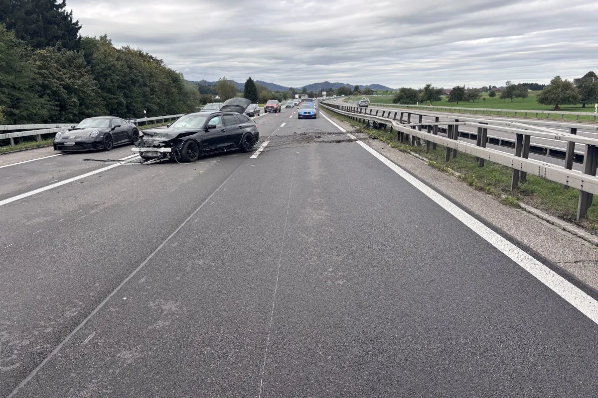 Mehrere Autos stehen auf einer Autobahn, darunter ein stark beschädigtes schwarzes Fahrzeug im Vordergrund. Die Straße ist gesperrt.