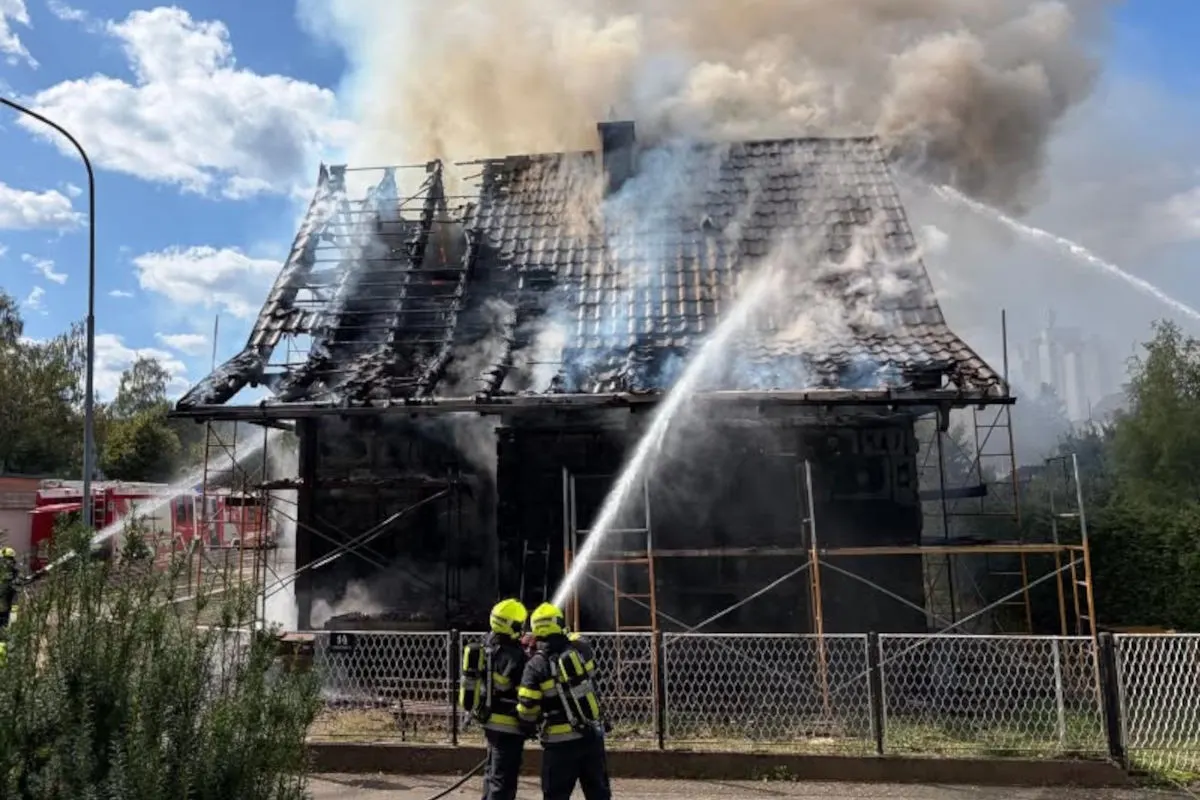 Ein stark beschädigtes Gebäude mit brennendem Dach, das von Feuerwehrleuten mit Wasserschläuchen gelöscht wird.
