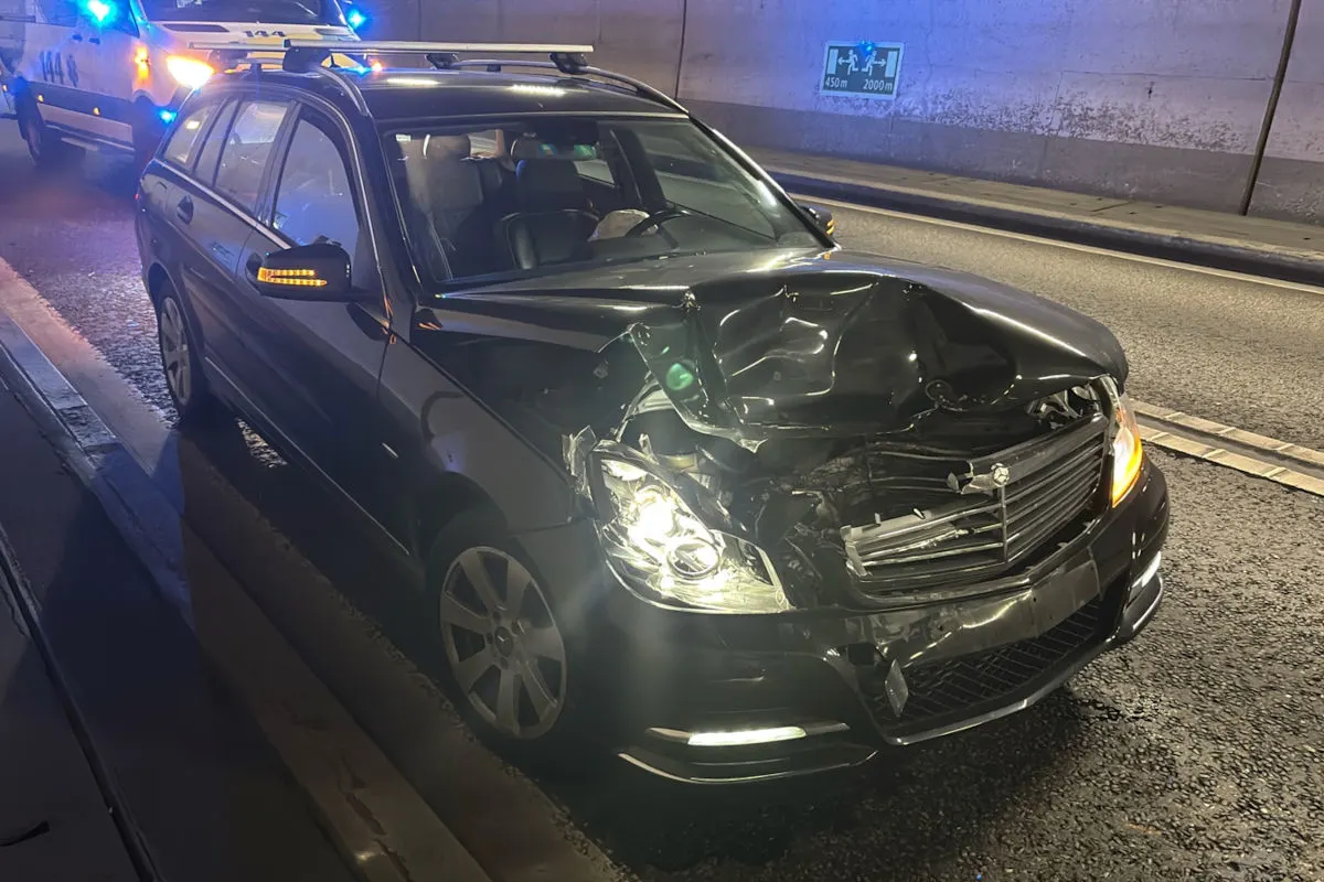 Ein schwarzer Mercedes mit stark eingedrückter Front steht in einem Tunnel. Ein Einsatzfahrzeug mit Blaulicht befindet sich im Hintergrund.