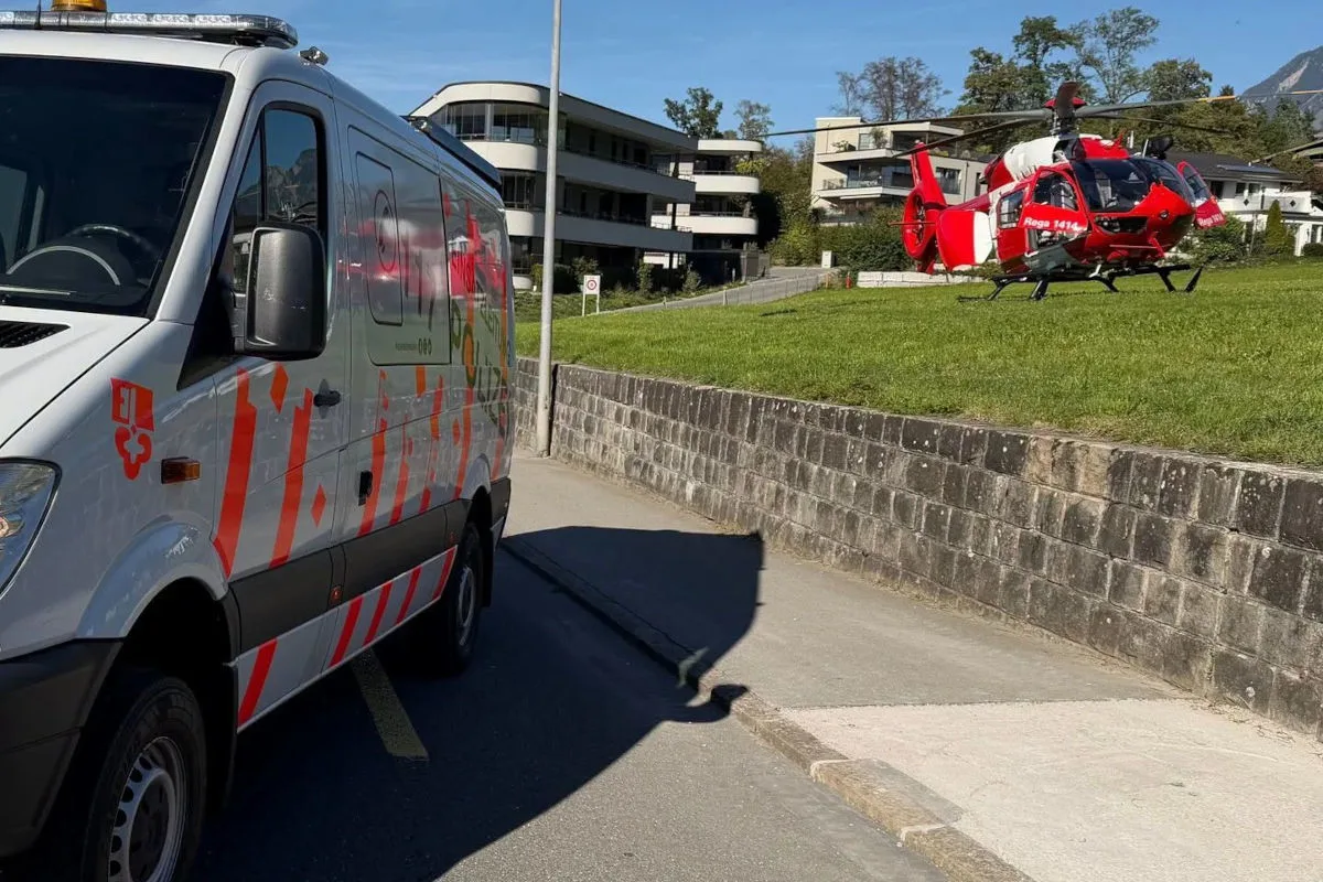 Ein roter Rettungshubschrauber ist auf einer Wiese gelandet, daneben steht ein weißer Feuerwehrwagen mit roten Markierungen. Im Hintergrund sind Wohngebäude zu sehen.