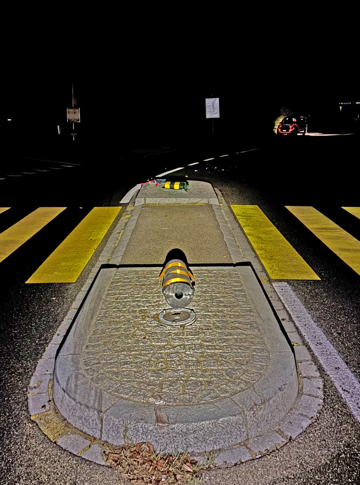 Eine Ampel liegt umgestürzt auf einem Mittelstreifen einer Straße. Im Hintergrund ist ein beleuchtetes Fahrzeug zu erkennen.