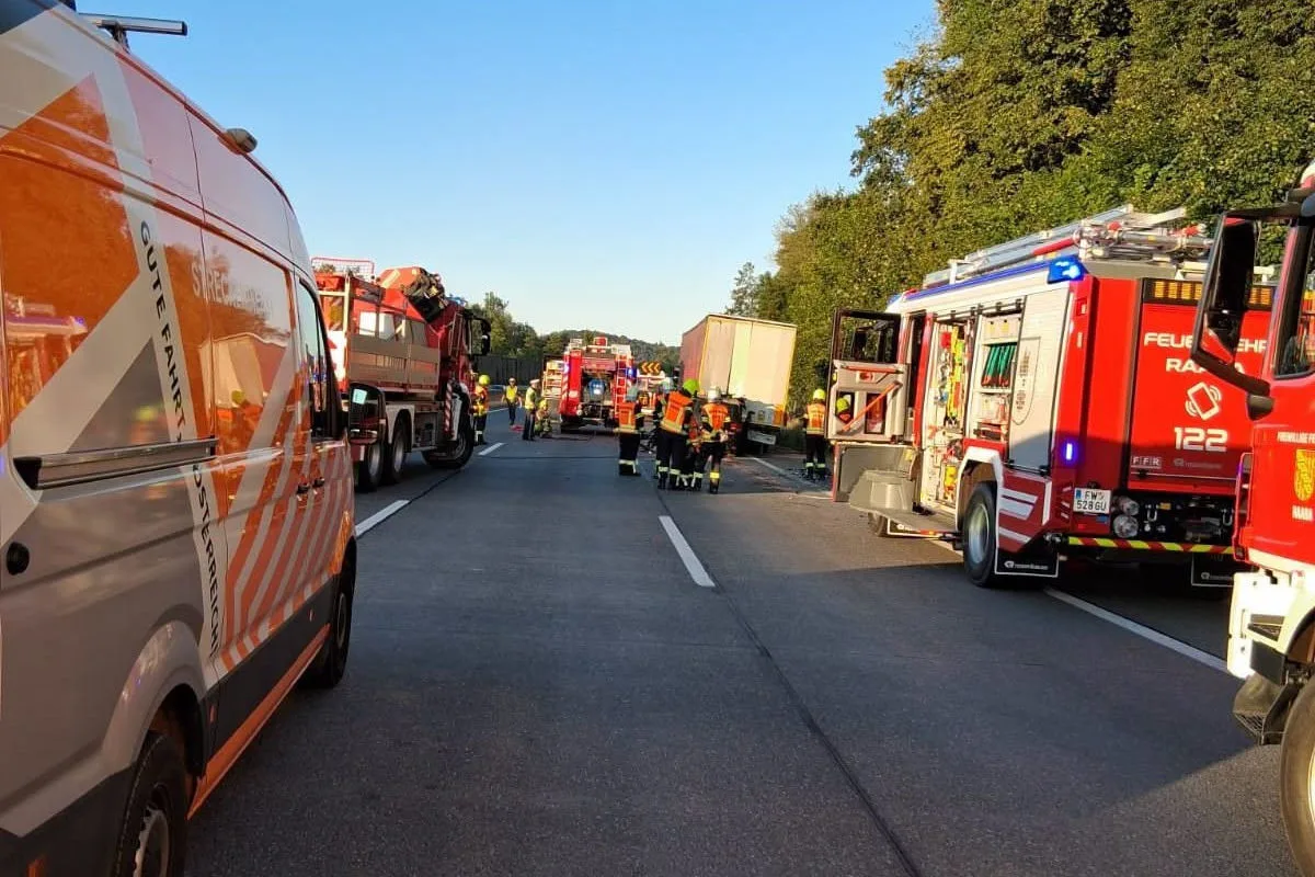 Mehrere Feuerwehrautos und Einsatzkräfte stehen auf einer Autobahn. Ein Lkw ist am Straßenrand zu sehen.