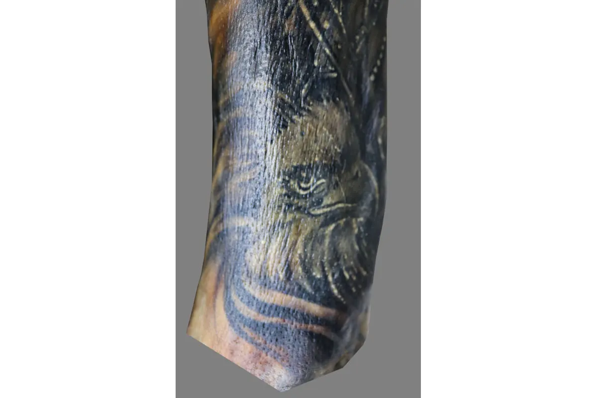 Ein Tattoo mit dem Motiv eines Adlers ist auf einem Arm zu sehen. Der Hintergrund ist neutral grau gefärbt.