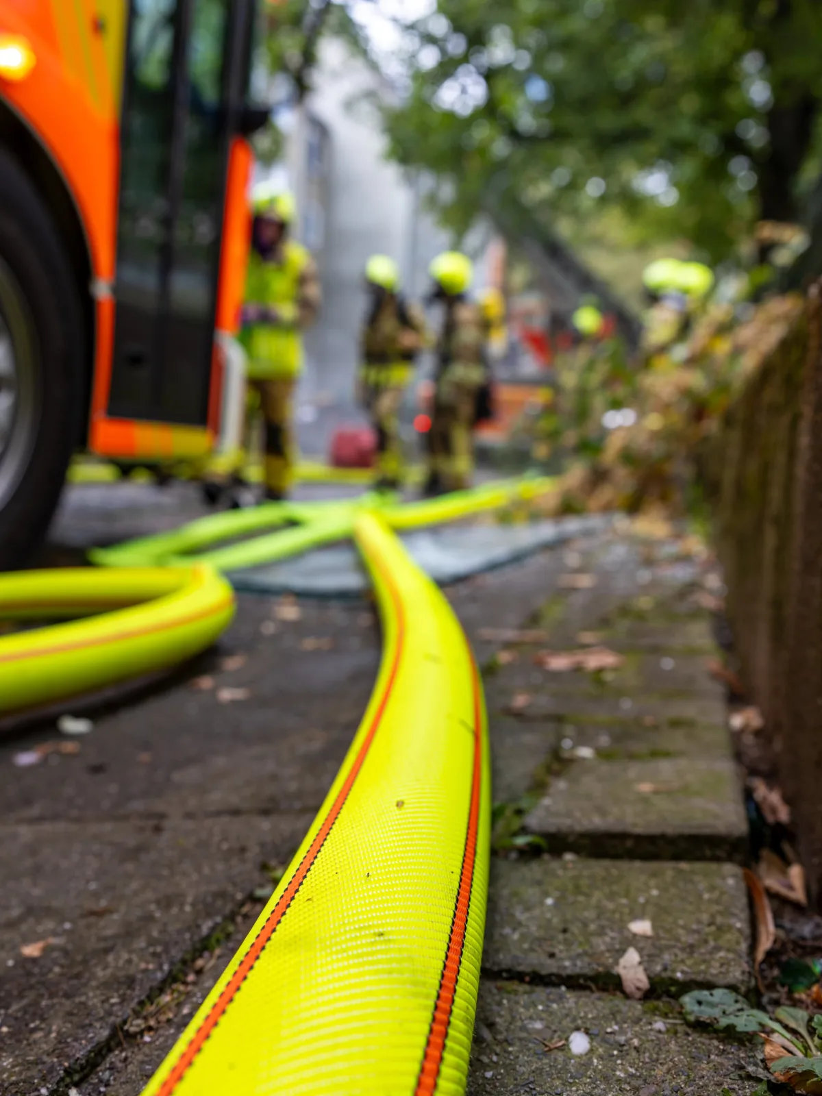 Mehrere Feuerwehrleute stehen mit gelben Schläuchen bei einem Einsatz draußen. Im Vordergrund liegt ein ausgerollter Feuerwehrschlauch auf dem Boden.