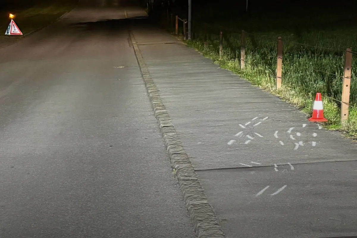 Eine nächtliche Straße mit Kreideumrissen auf dem Gehweg sowie einem roten Warnkegel. Die Umgebung ist schwach beleuchtet.