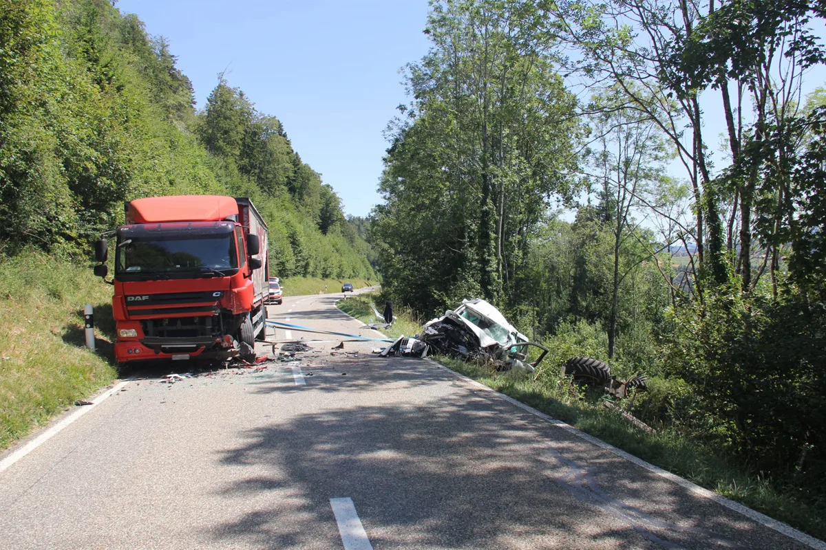 Ein roter Lkw steht nach einer Kollision am Straßenrand, daneben abgestürzter Traktor in der Böschung.
