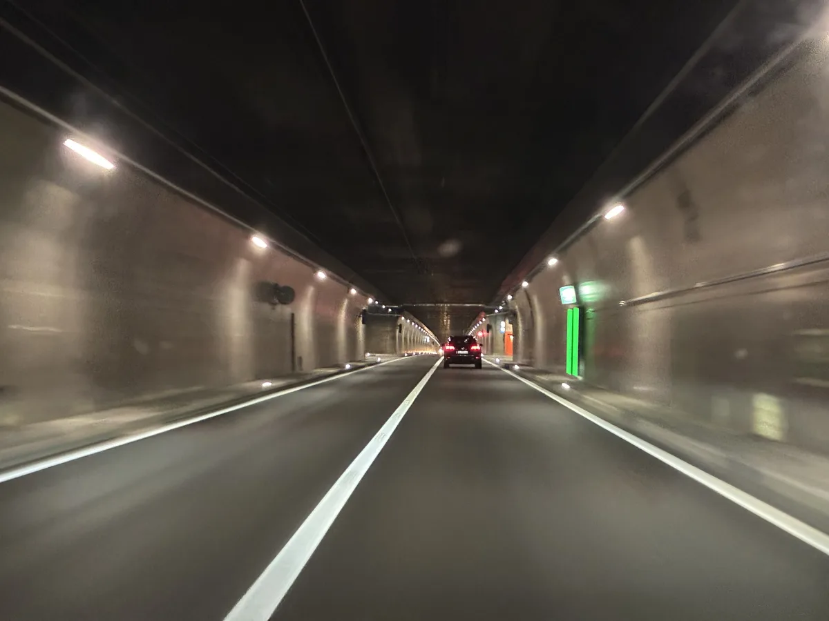 Ein Auto fährt auf einer geraden Strecke durch einen gut beleuchteten Tunnel. Die Tunnelwände sind mit Lichtern versehen, die den Weg erhellen.