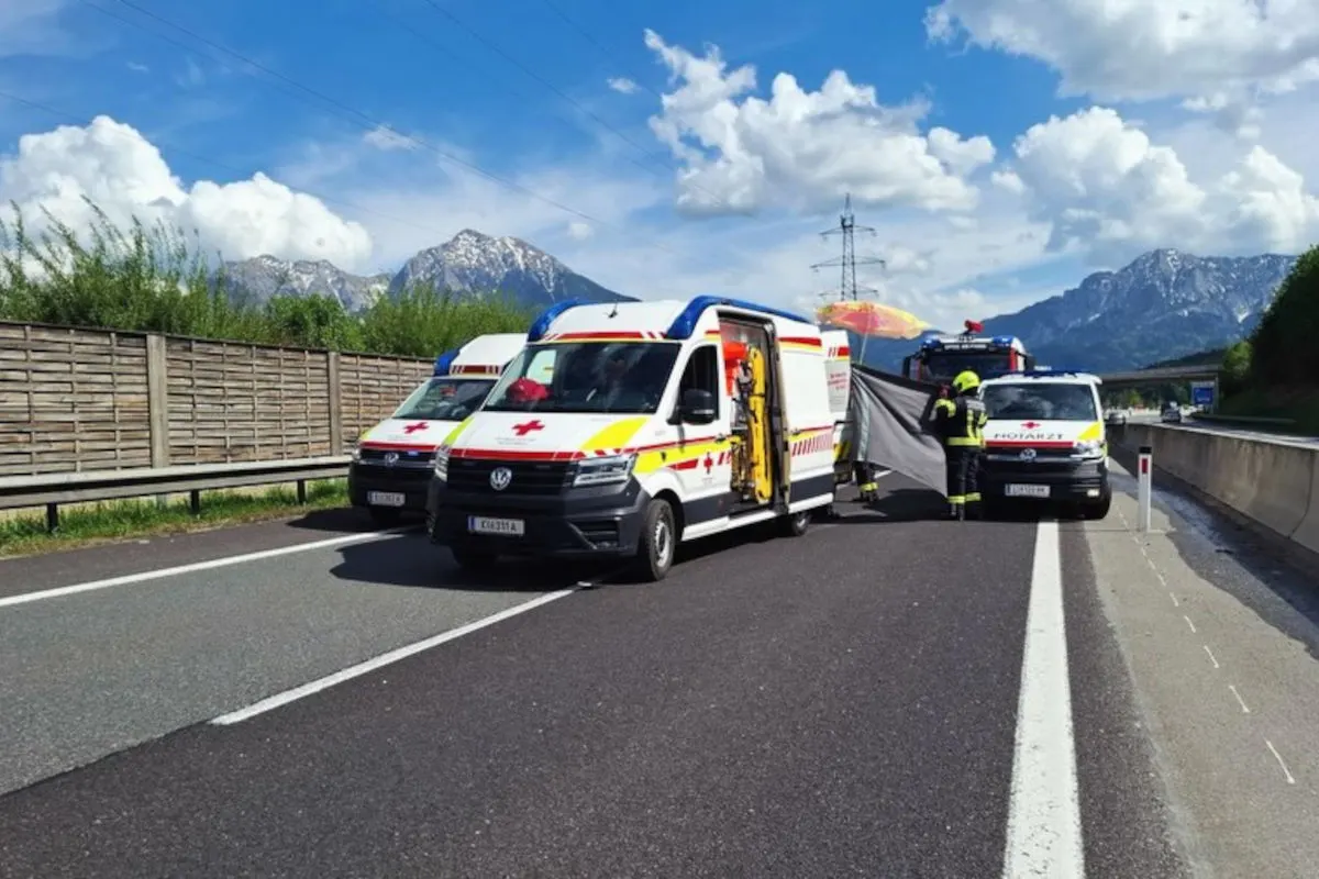 Mehrere Rettungsfahrzeuge parken auf einer Autobahn. Im Hintergrund sind Berge und eine klare, sonnige Himmel zu sehen. Einsatzkräfte stehen neben einem offenen Rettungsfahrzeug.