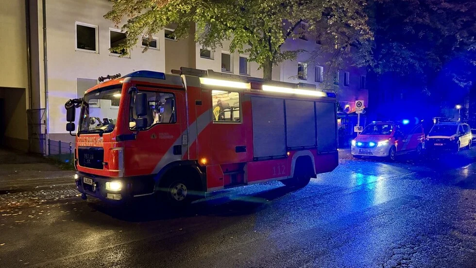 Ein Feuerwehrauto steht bei Nacht auf einer nassen Straße. Im Hintergrund sind weitere Einsatzfahrzeuge mit eingeschaltetem Blaulicht zu sehen.