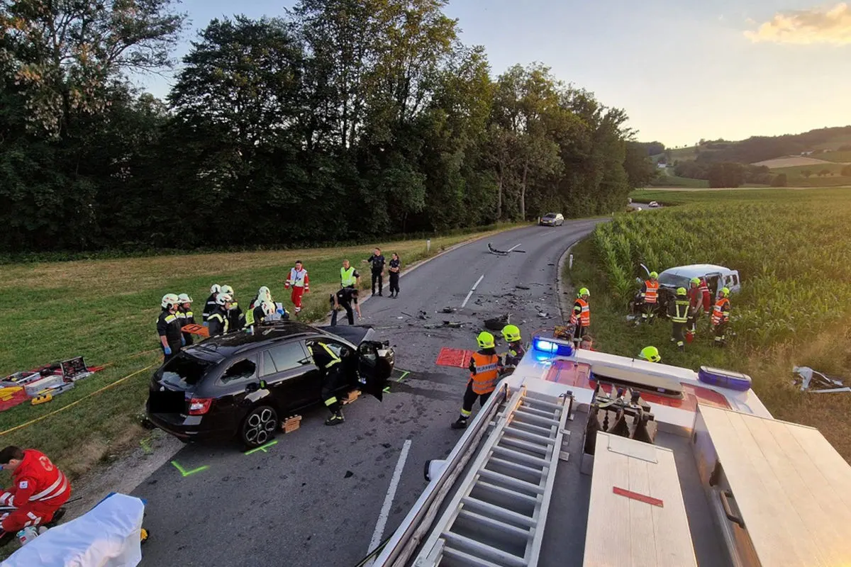Eine Unfallstelle auf einer Landstraße, mehrere Einsatzkräfte arbeiten um ein beschädigtes schwarzes Auto herum. Ein weiteres Fahrzeug steht in einem Feld.