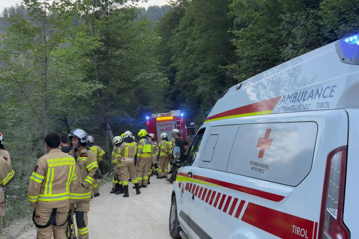 Mehrere Feuerwehrleute in Einsatzkleidung stehen neben einem Ambulanzfahrzeug und einem Feuerwehrwagen im Wald.