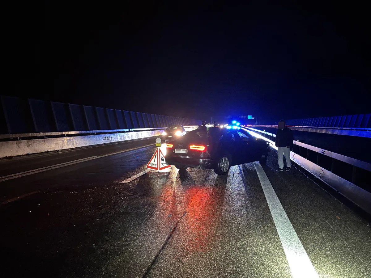 Ein Auto steht quer auf der Fahrbahn einer Brücke, umgeben von Polizeifahrzeugen mit eingeschaltetem Blaulicht in der Nacht.