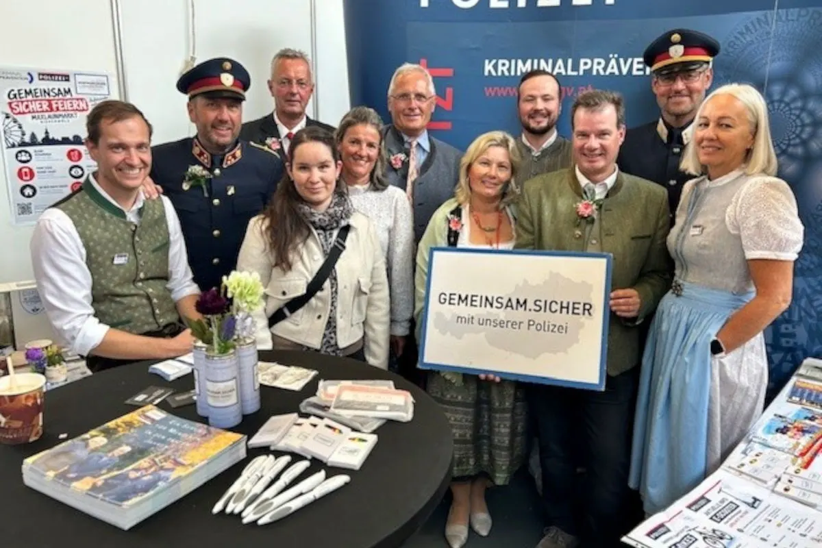Eine Gruppe von Menschen in traditioneller Tracht steht gemeinsam an einem Informationsstand der Polizei mit einem Plakat im Vordergrund.